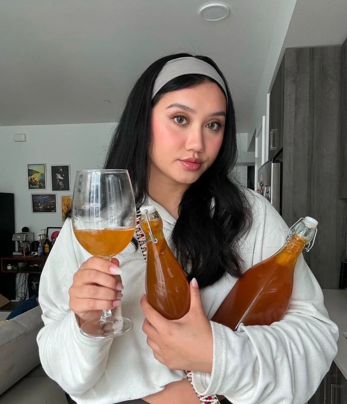 Angela holding a glass and two bottles of an amber drink