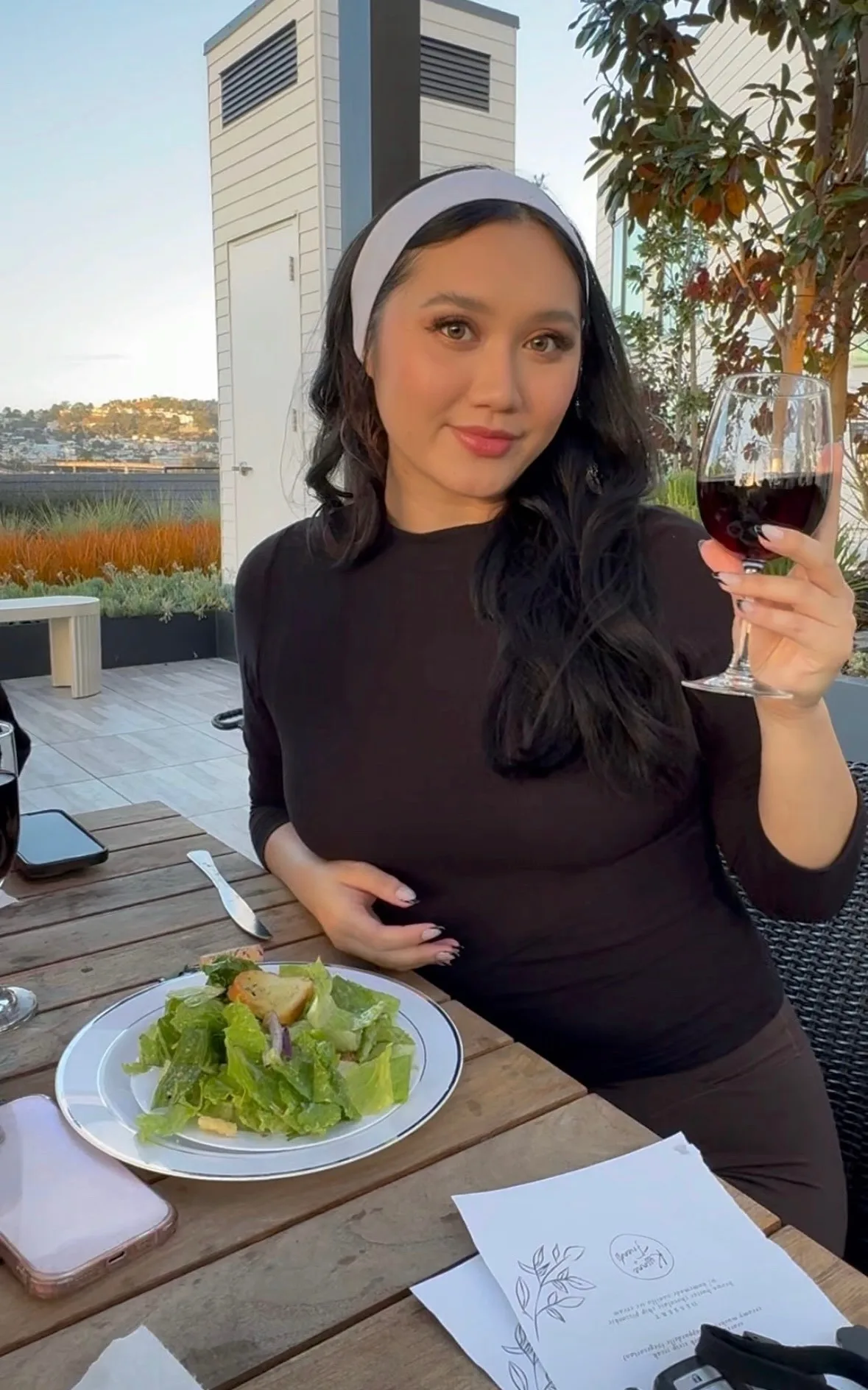 Angela seated at an outdoor restaurant table with a glass of wine