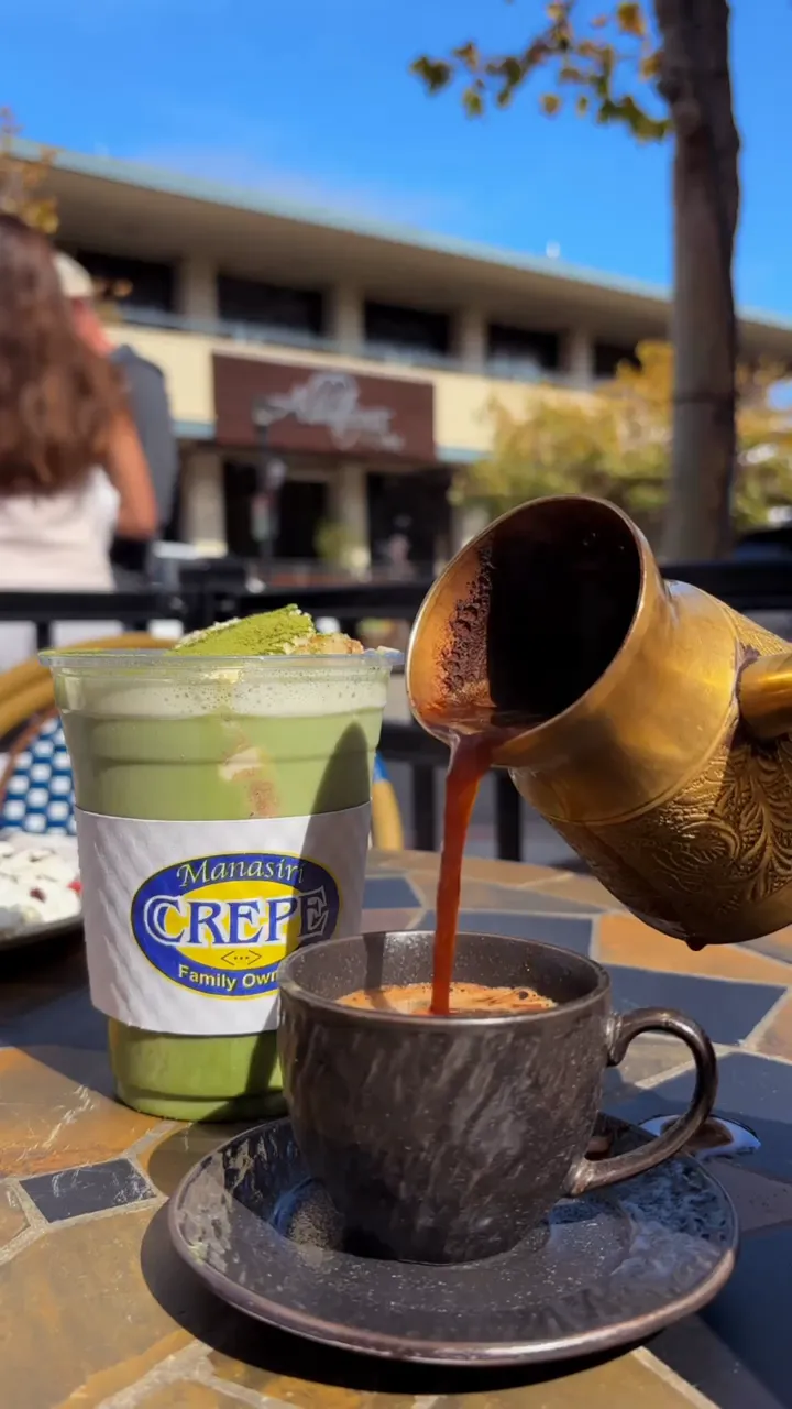 Coffee being poured beside an iced matcha at an outdoor cafe table